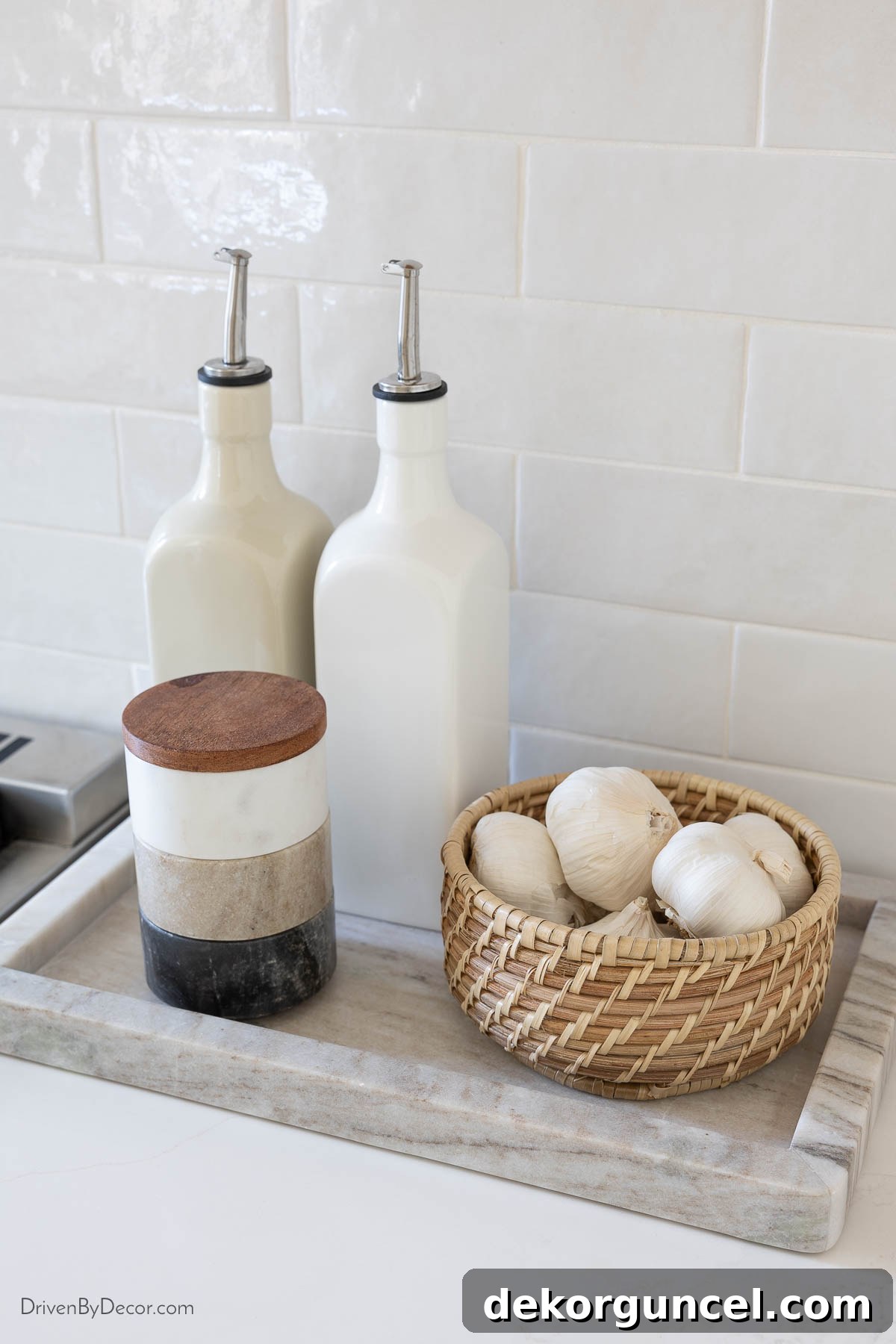 Marble tray next to the range, neatly organizing ceramic oil dispensers, stacking spice pots, and a woven basket for garlic