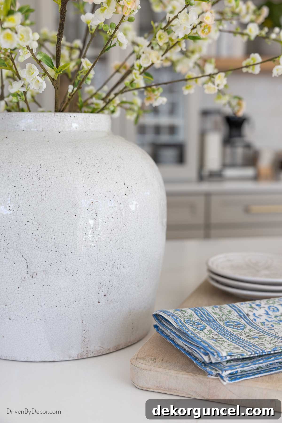 Large white vase with a distinctive crackle finish, elegantly holding faux spirea branches on the kitchen island