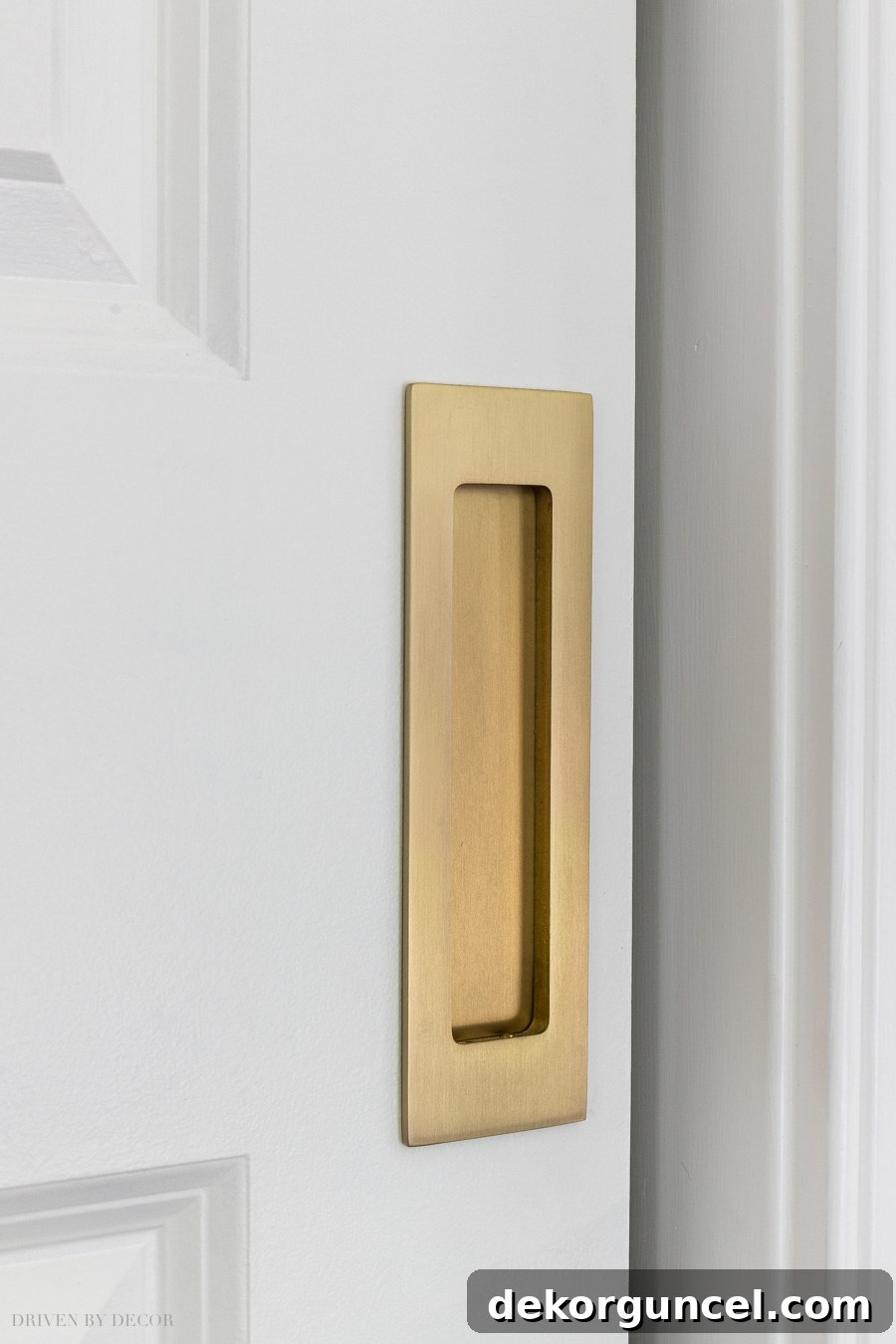 Close-up of a satin brass rectangular flush pull on a pocket door, enhancing the entryway to an IKEA PAX walk-in closet.