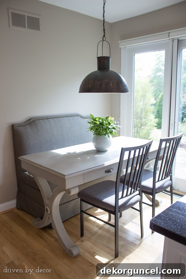 A cozy eat-in kitchen area featuring an upholstered banquette, a desk repurposed as a dining table, and stylish pendant lighting, creating a spacious feel.