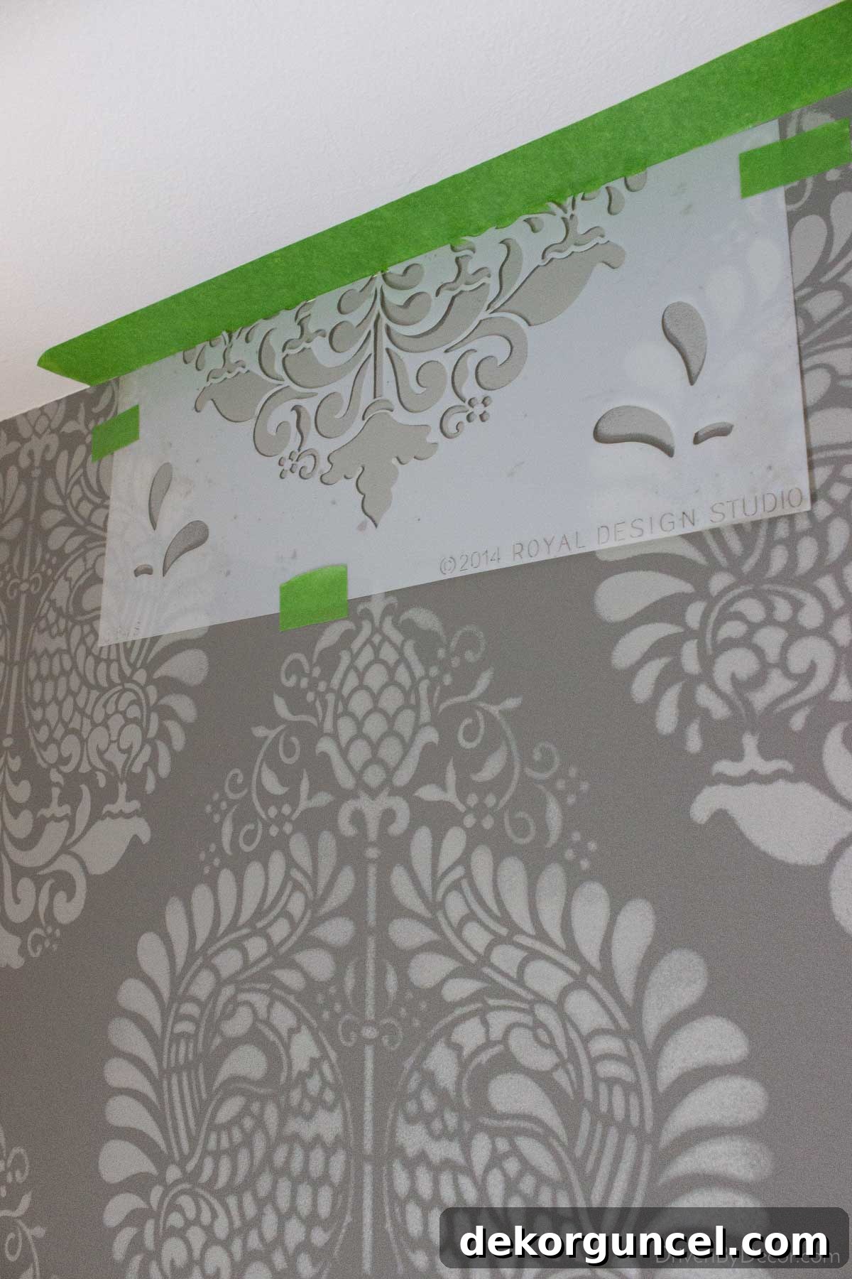 Şablonla Duvarlarınıza Hayat Verin: Büyüleyici Alanlar Yaratın 12 Illustrates the process of stenciling the top edge of a wall, demonstrating how to achieve a clean line where the pattern meets the ceiling.