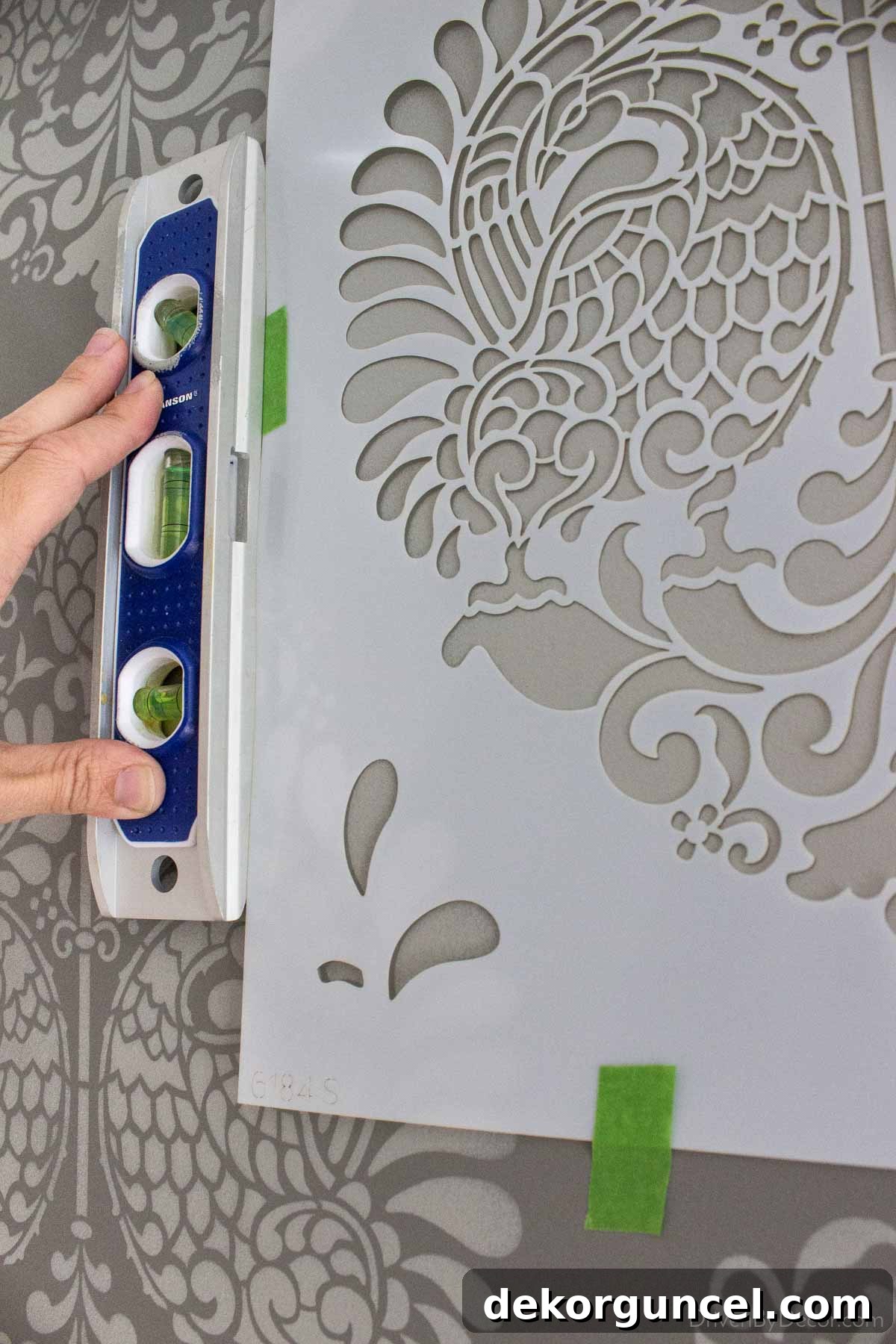 Şablonla Duvarlarınıza Hayat Verin: Büyüleyici Alanlar Yaratın 9 The initial application of a wall stencil, carefully leveled and taped to the wall, demonstrating the foundational step for a precise pattern.