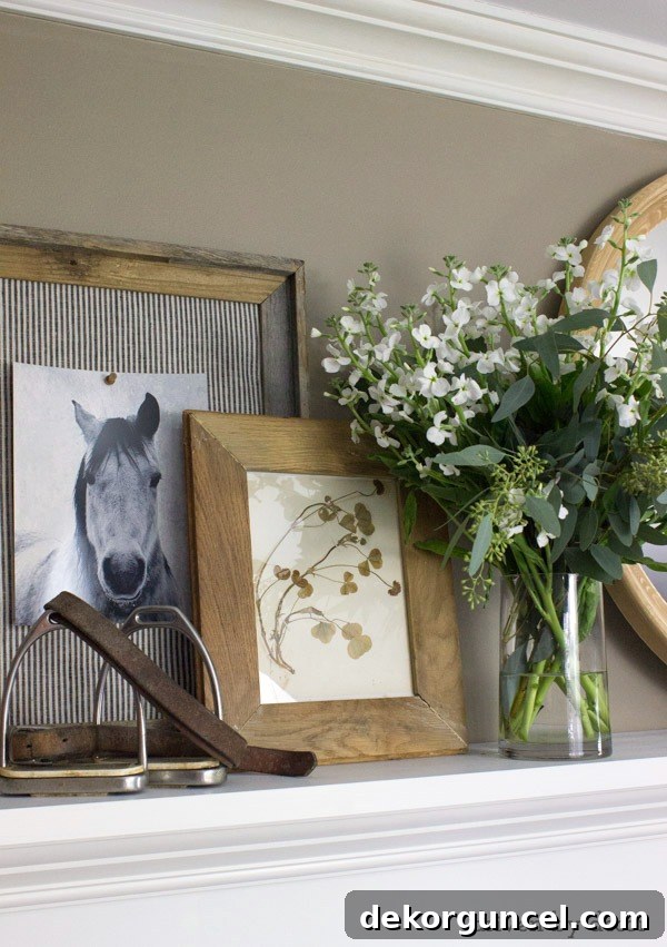 Beautifully styled fireplace mantel with layered artwork, a round mirror, and fresh flowers