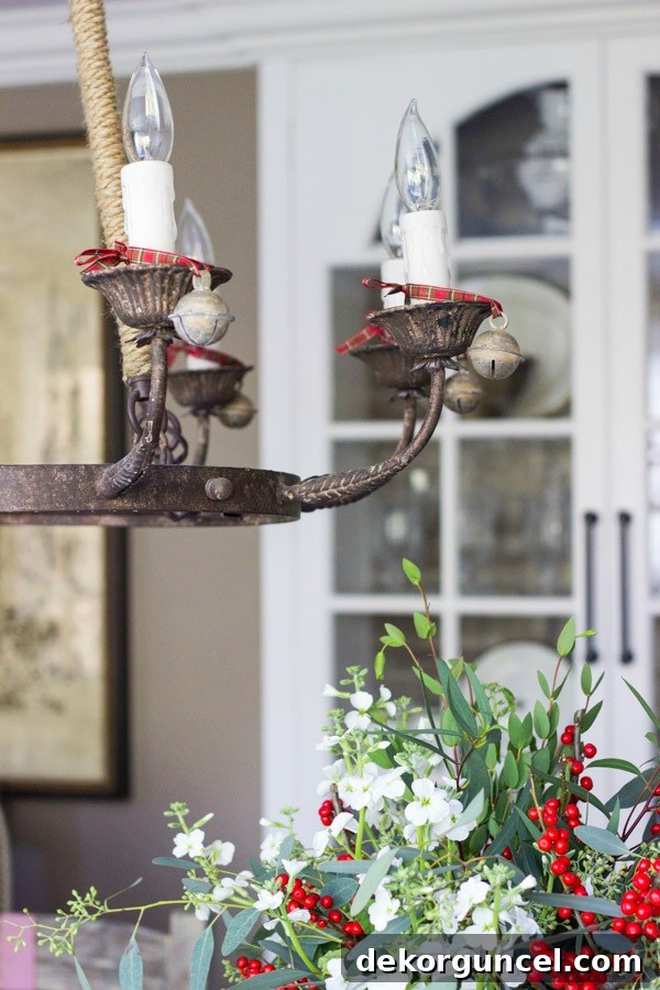 Quintessential New England Christmas Style 16 Vintage-style bells elegantly tied onto a chandelier with ribbon, lending festive charm and a touch of antique allure to this dining room, beautifully decorated for the holidays.