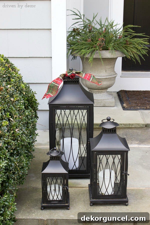 Quintessential New England Christmas Style 3 Simple holiday decorations for your front porch featuring large urns brimming with greenery and berries, alongside two sets of black lanterns adorned with holiday ribbon, creating a welcoming and elegant entrance.