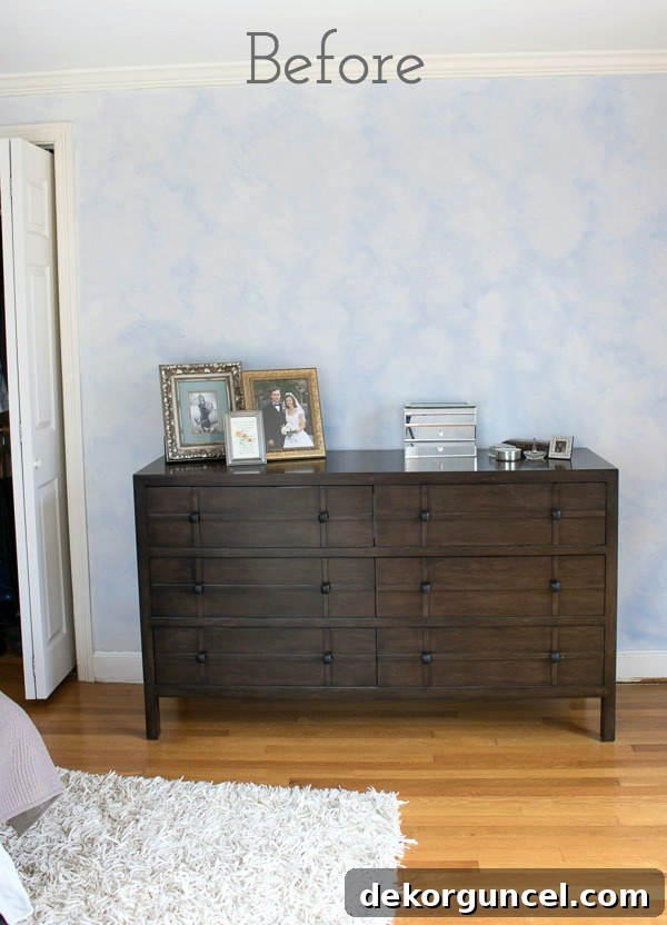 The master bedroom dresser before its significant makeover, showing a dark, dated wooden dresser with a completely blank wall above, highlighting the room's uninspired aesthetic.