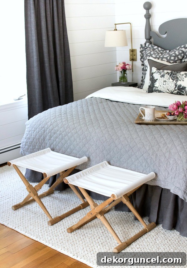 A tasteful pair of camp stools strategically placed at the foot of the bed, offering a practical and stylish solution for stacking bed pillows at night and providing a convenient seat for morning routines.