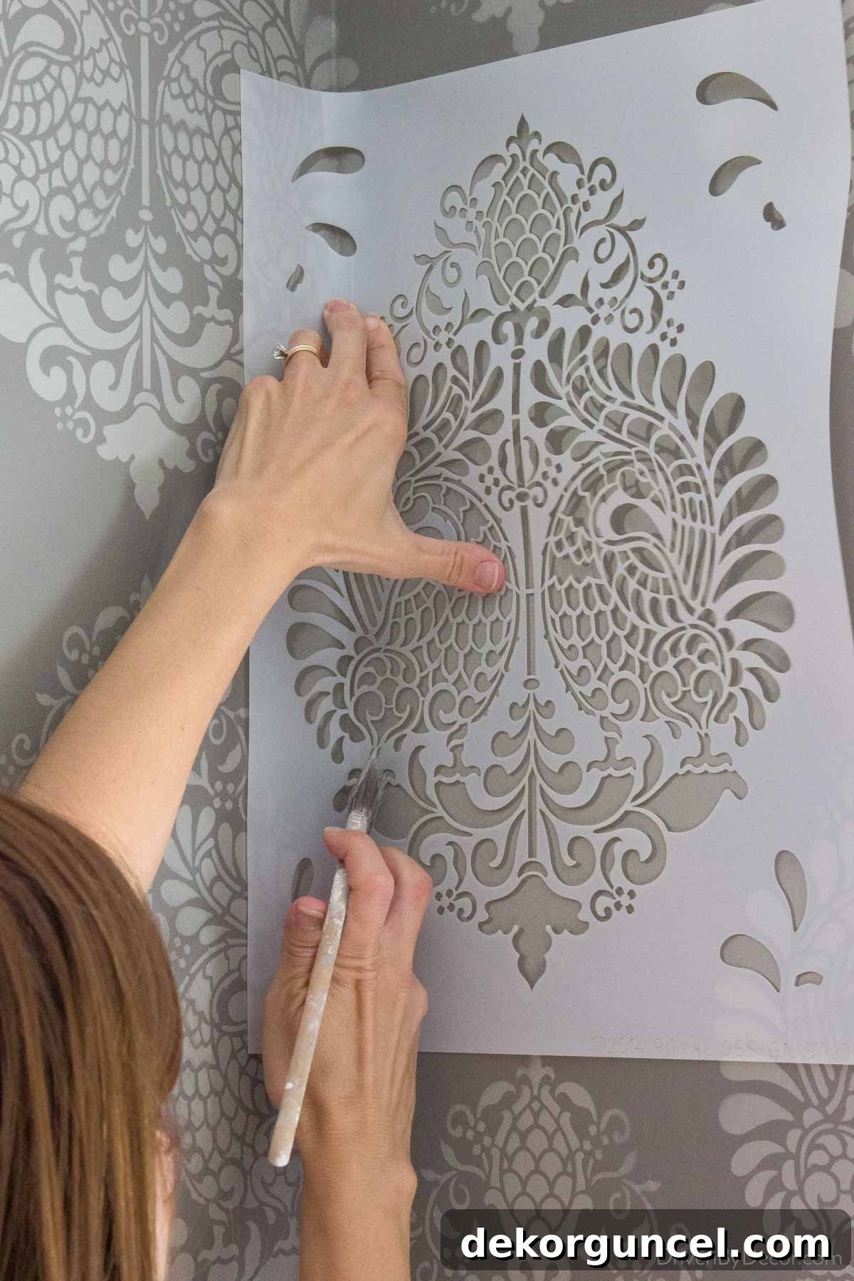 My Top 10 DIY Home Projects 5 Close-up image of the stenciling process in a bathroom corner, showing intricate damask pattern being applied to a dark gray wall with light gray paint.