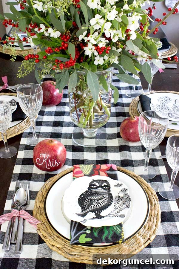 Holiday placesetting with floral centerpiece, pomegranate place cards, silverware tied with ribbon, buffalo check runner, and festive plates