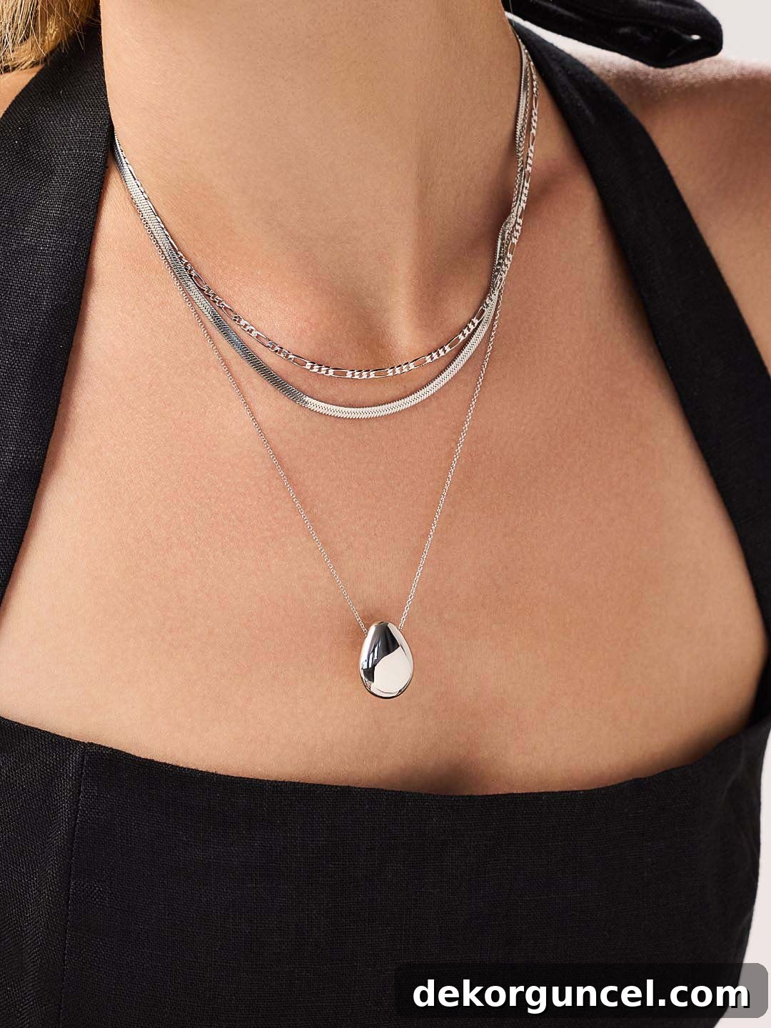 Elegant silver pendant necklace layered with other delicate chain necklaces, showcasing a classic style.