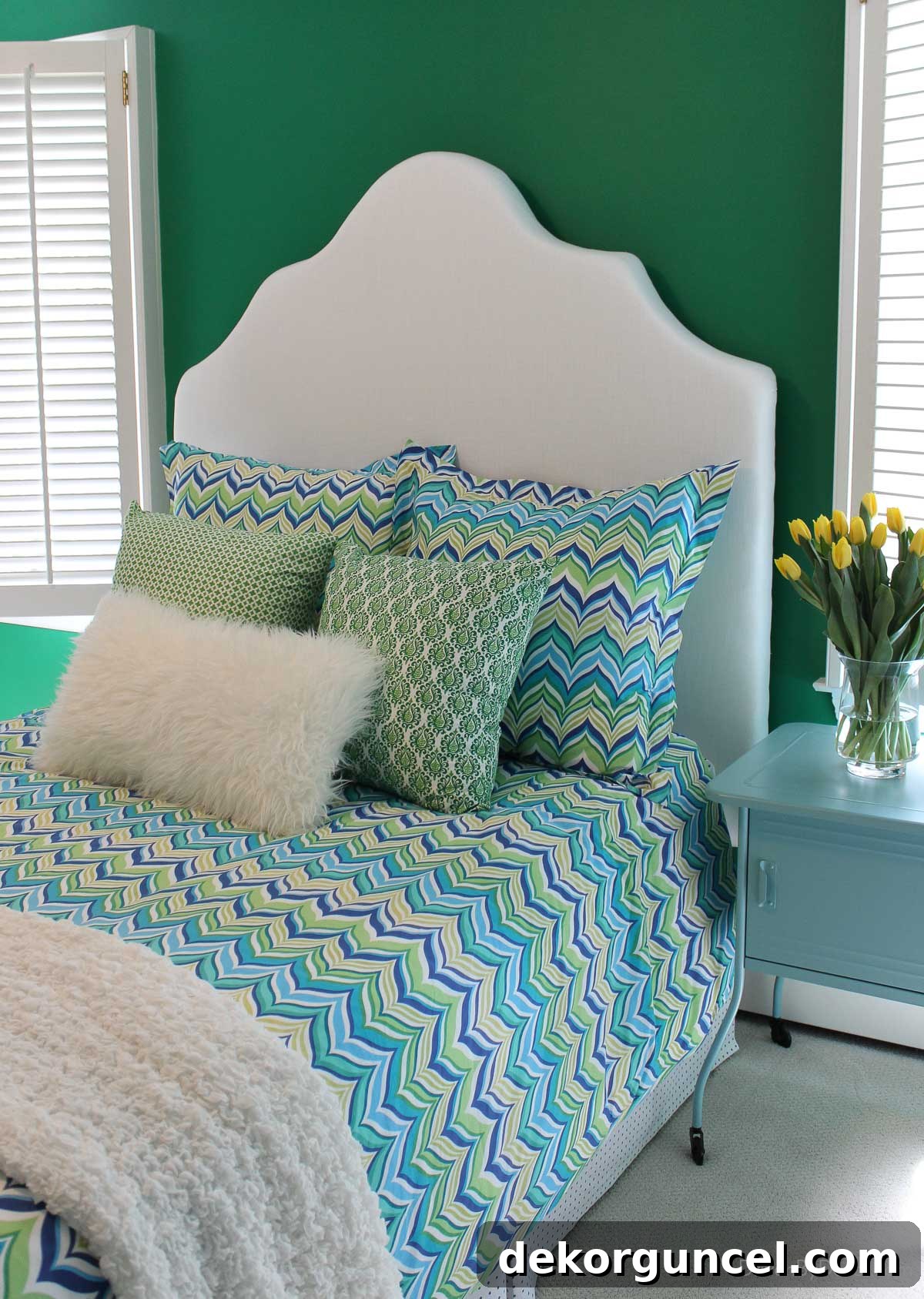 Finished DIY upholstered bed in bedroom with green, blue, and yellow bedding